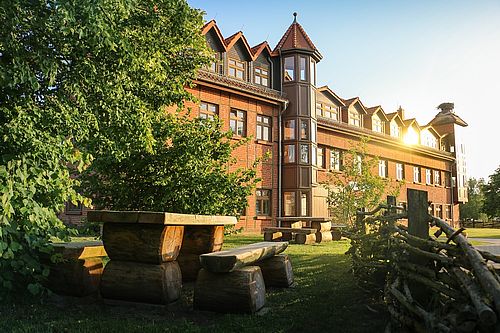 Tisch aus massivem Holz vor einem großen solitären Haus aus Backstein.