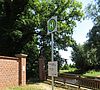 Blick auf eine kleine Brücke mit Infotafel in einem grünen Park mit Bäumen.