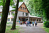 Zwischen alten Bäumen liegt das Gästehaus. Eine Gruppe junger Mensch kommt vom Gästehaus her und ist auf dem Weg zum Wasser.