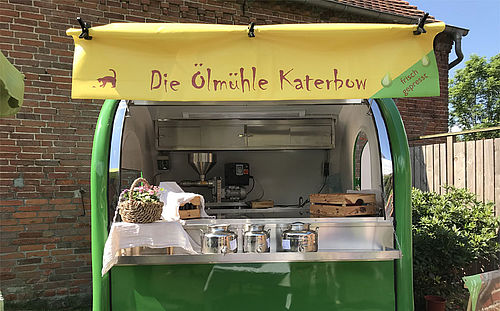 der grüne Anhänger mit gelben Dach als Verkaufsstand der Ölmühle Katerbow