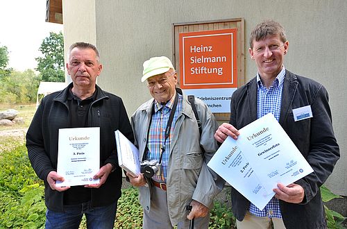 Drei Männer halten Urkunden in den Händen.
