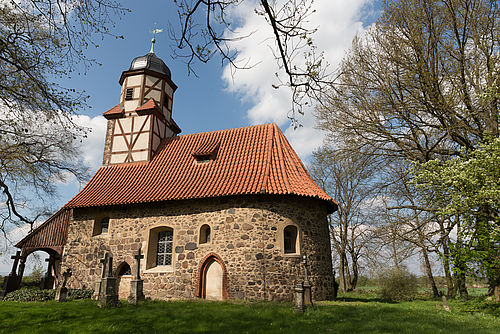 Eine Kirche aus Feldstein auf einem kleinen Hügel umgeben von Bäumen.