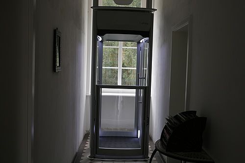Ein moderner Fahrstuhl aus Glas in einem Hausflur.