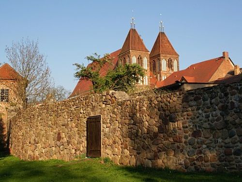 Die von der Abendsonne angestrahlte alte Stadtmauer mit einer kleinen Tür wird von den zwei Türmen der die große St. Nikolai-Kirche überragt.