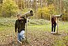 Zwei Personen halten ihr Ohr an einen Hörtrichter, im Hintergund bunter Herbstlaubwald