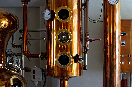 Die Destille ist kupferfarben und besteht aus mehreren Behältern, die über Rohre miteinander verbunden sind.