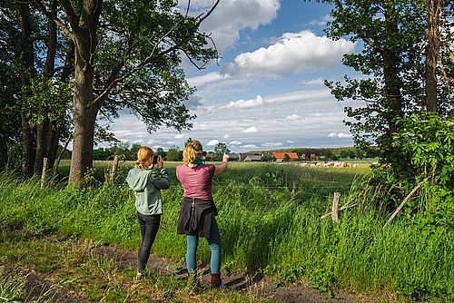 Zwei Frauen im vordergrund schauen auf eine Weide mit einer Dorfsilhouette im Hintergrund