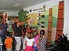 eine Frau zeigt einer Gruppe Kinder etwas an einer mit Karte, Bildern und Zeichnungen gestalteten Wand