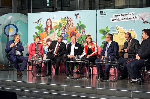 Podiumsmdiskussionsrunde mit vielen Teilnehmern.