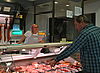 An der Theke wählt ein Kunde aus den verschiedenen Fleisch- und Wurstwaren und wird dabei von einer freundlichen Mitarbeiterin beraten.