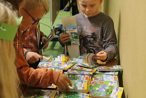Mehrere Kinder stehen um einen Tisch herum und suchen sich kleine Hefte mit Geschichten aus 